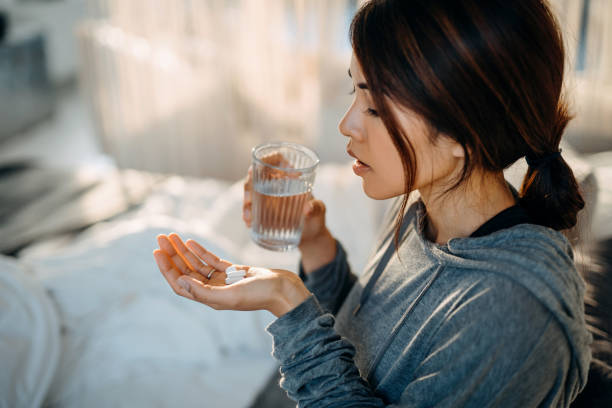 A young woman is holding medication in her hand and a glass of water in her other hand.