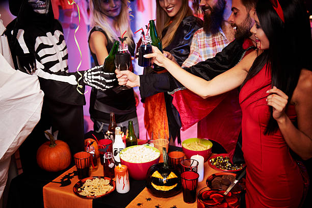 In this image we see a Halloween party happening, as all of the guests stand over the table doing a cheers with their drinks.