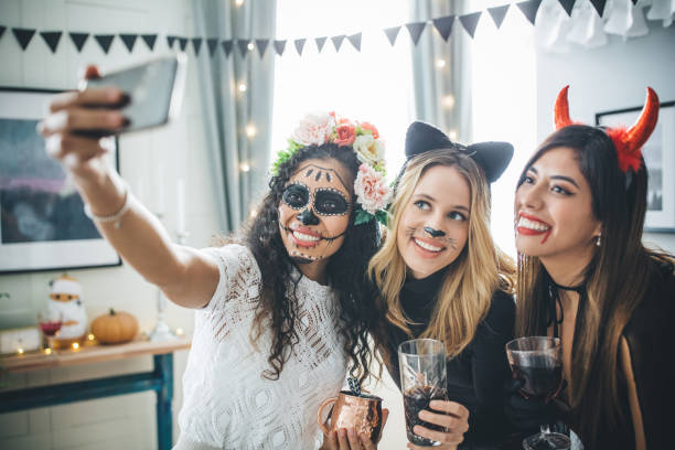 Three young women are all dressed up in costumes for a Halloween party. They each have a drink in their hand as they take a selfie together.