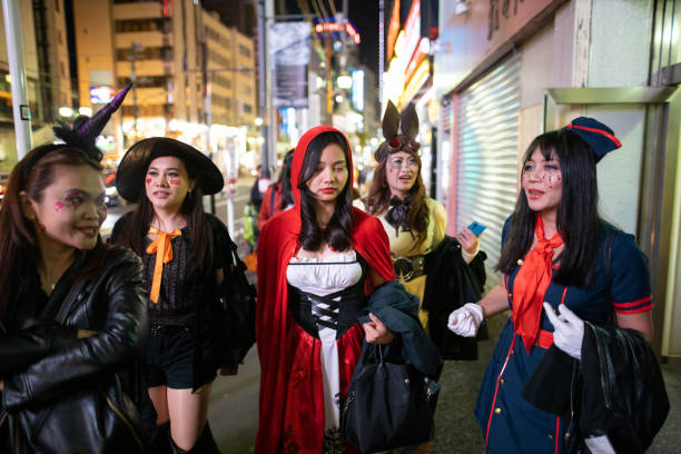 In this image, 5 Asian American women are all dressed up in costumes for Halloween as they walk down the street beside each other.