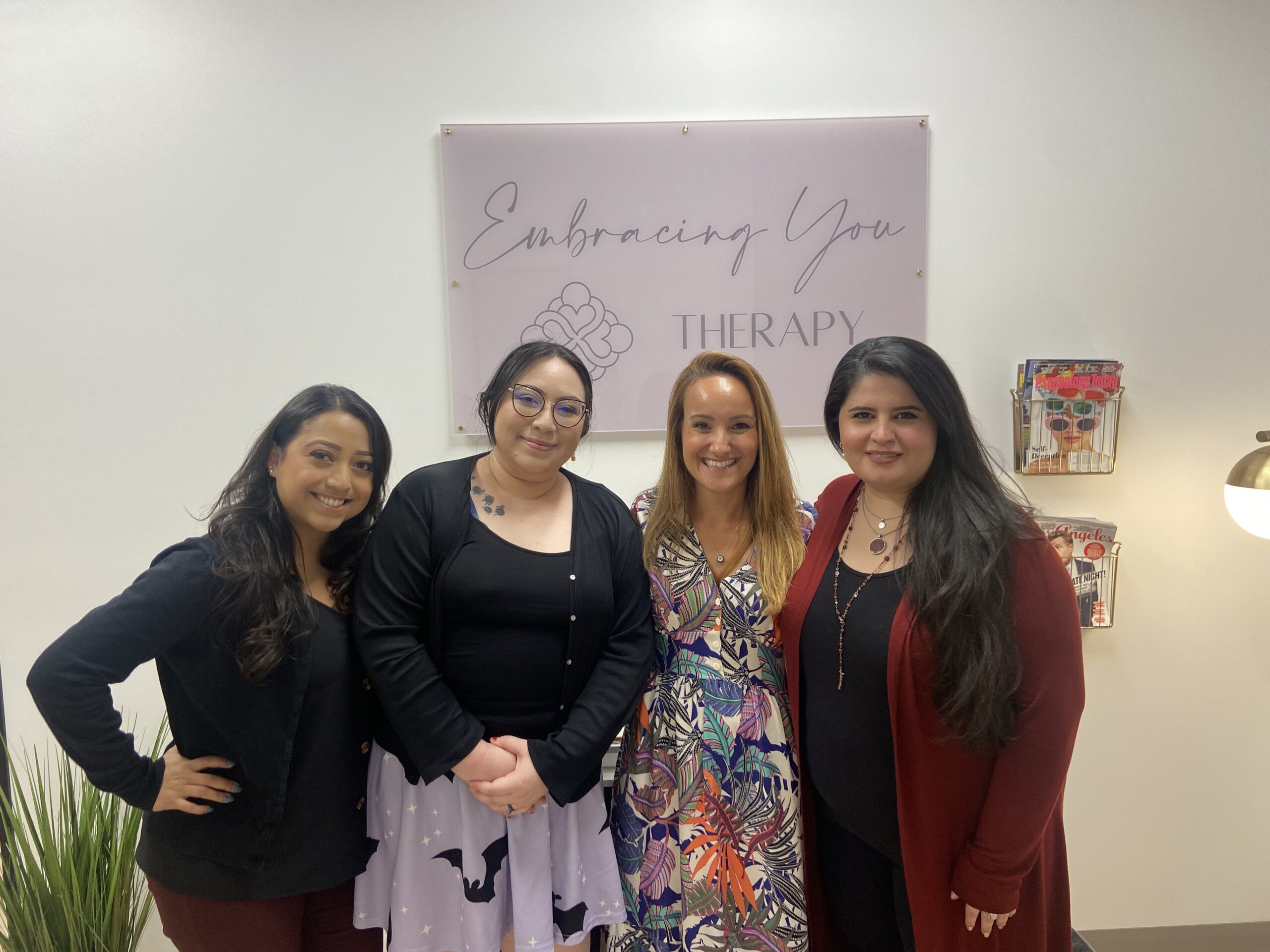 Therapist team smiling and posing for a photo in front of a sign that reads, Embracing You Therapy.