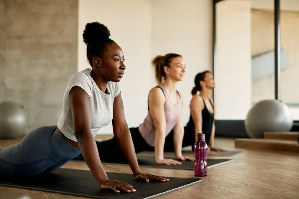 Three young women are in a yoga class, doing a yoga pose on a yoga mat. 