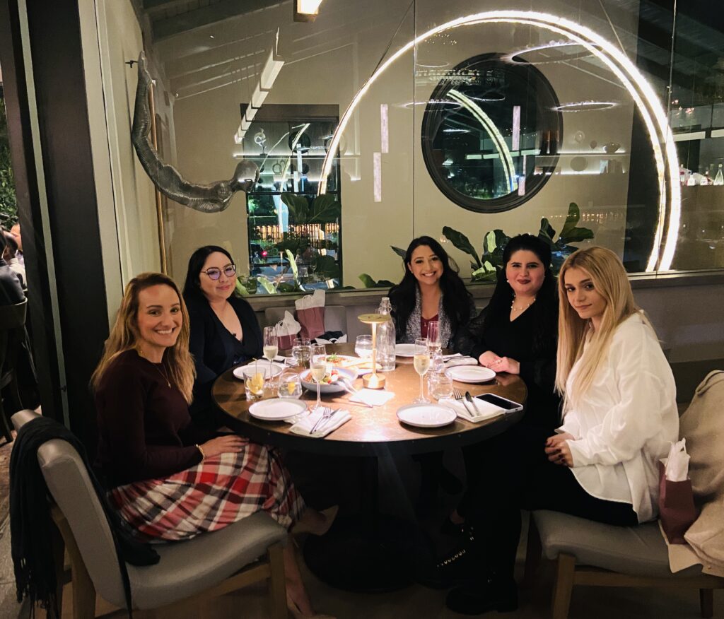 Therapist team smiling and enjoying a meal together at a restaurant, engaged in conversation and savoring their time together.