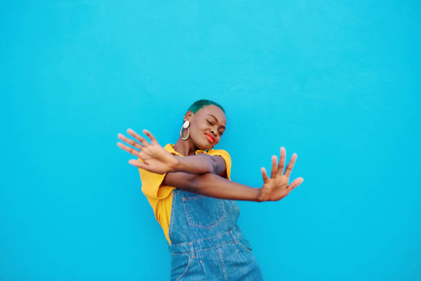 A young African American woman is standing in front of a blue background. She is holding her hands out in front of her with a smile on her face.