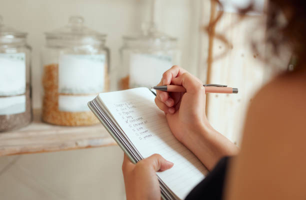 A woman is writing in her journal with a pen. She is standing in her pantry.