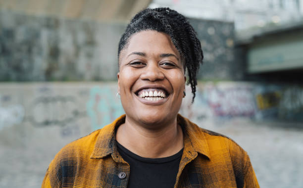 An African American non-binary individual is standing in front of the camera smiling largely. She is very happy.