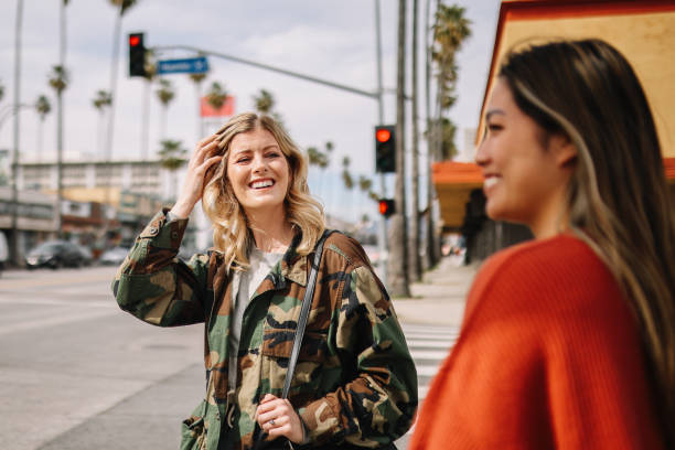 Two young women are walking together on the busy streets of Los Angeles. Both of the women are smiling at each other.