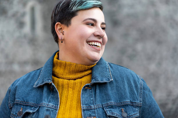 A non-binary woman is standing outside smiling as she looks to her left. 