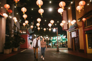 A young couple is taking a walk in Chinatown in Los Angeles at night. They are holding hands and smiling together.