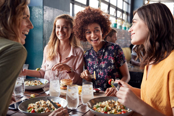 A group of 4 women are having dinner together at a restaurant. They are all laughing and smiling together. These may be coworkers grabbing lunch during work.