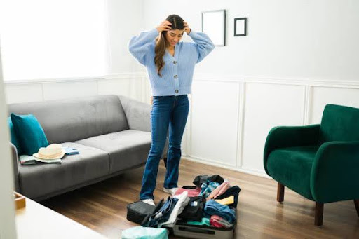 Anxious worried woman looking disorganized while preparing her clothes and suitcase before going on a trip alone