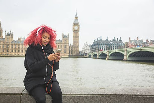 Beautiful redhair woman listening music in London with Big Ben and Westminster palace on background. She wear fashion white headphones.
