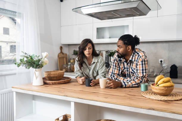 Young couple drinking coffee together in the kitchen on early morning before they go to the work. Emotional people spending free time with tea and conversation.