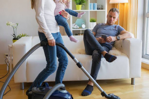 Woman with small child in her hands doing housekeeping while man sitting in couch and relaxing. Relationship Has Become Transactional