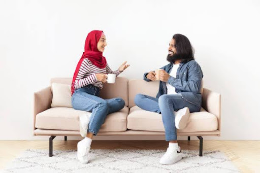 Cheerful Young Muslim Couple Resting Together At Home, Drinking Coffee And Chatting While Sitting On Comfortable Couch In Living Room, Happy Islamic Spouses Enjoying Domestic Leisure, Free Space Relationship Has Become Transactional