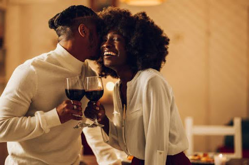 Portrait of a cheerful happy african american couple drinking wine and having romantic evening at home while kissing and bonding together. Home date night, clinking wine glasses. Relationship Has Become Transactional