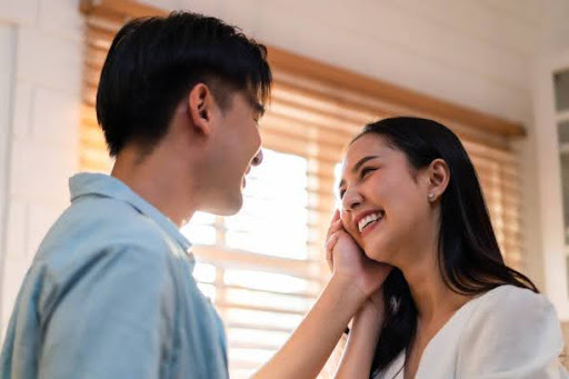 Asian young man and woman looking each other in living room at home. Attractive romantic new marriage couple male and female spend time celebrate anniversary and valentine's day together in house.