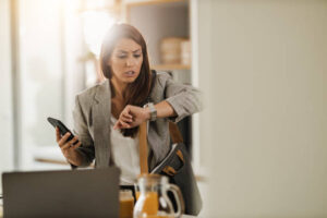 A young business woman is in her kitchen as she looks at the watch on her hand. She is running late from work.