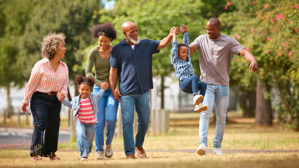 A young African American couple is on a walk with their two children and their parents. The 6 of them are walking in a park side by side.