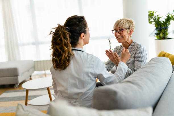 A mother and daughter are sitting on the couch together as they talk. They are both smiling as they have a conversation.