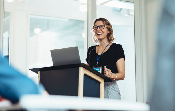 A young woman is standing at a podium giving a presentation. She has her laptop open in front of her. 