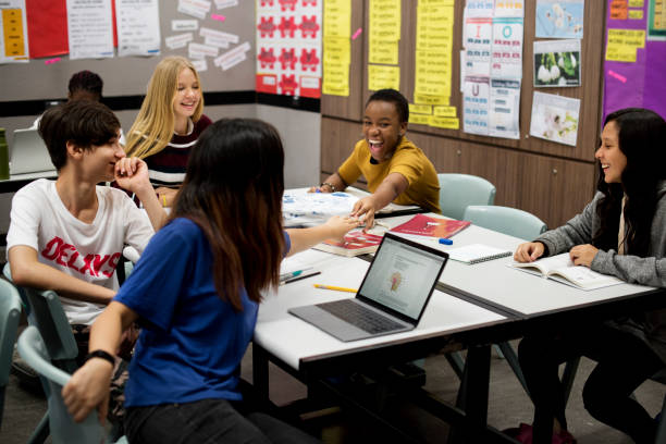 A group of 5 students are sitting together in a classroom. They are are laughing and smiling.