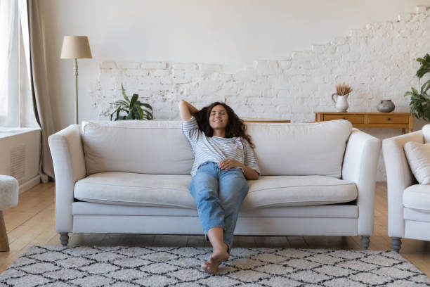 A young biracial woman is laying on her couch with her eyes closed. Her hand is behind her head as she rests.