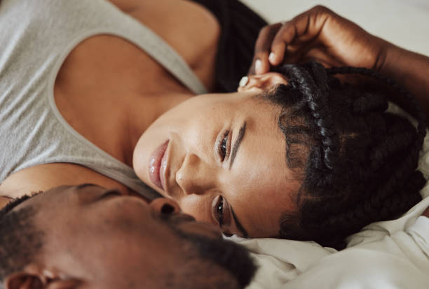 An African American couple is laying down together looking into each others eyes. The man has his hand on her head as he smiles.