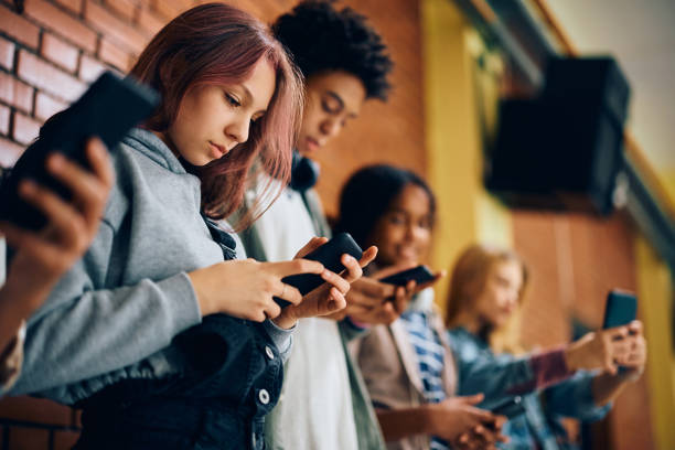 A group of 4 teenagers are standing beside each other looking at their phones.