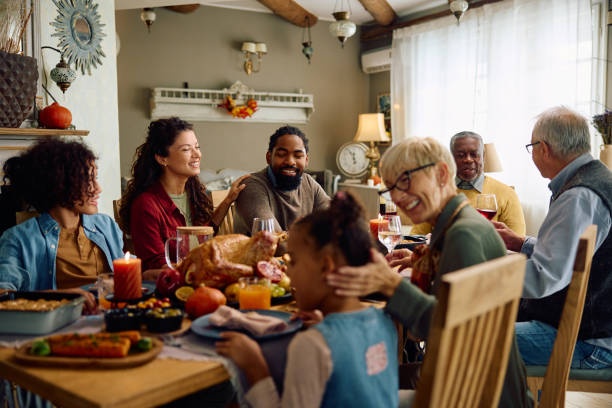 A biracial family is sitting down together for Thanksgiving dinner. They are all smiling and laughing together.