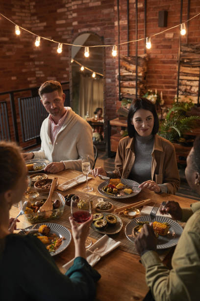 Four friends are having Thanksgiving dinner together in their dining room. The two couples are sitting across from each other as they converse.