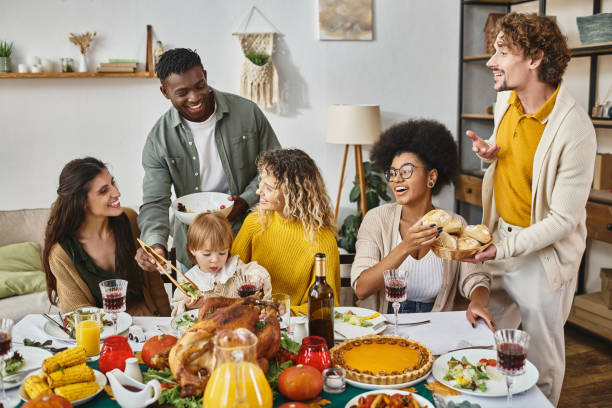 A biracial family is sitting together on the dinner table on Thanksgiving. They are sharing meals together as they laugh and smile.