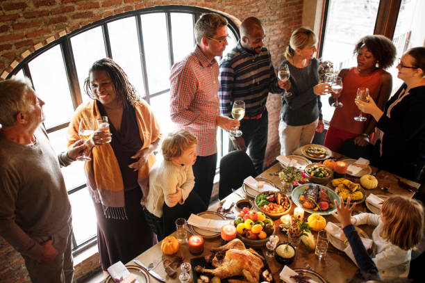 A large group of friends are having a Thanksgiving dinner together. They are all standing around the dinner table with wine glasses.