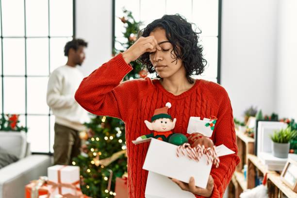 An African American woman is decorating her home with Holiday decorations with a stressed look on her face.