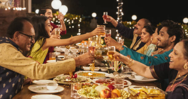 An Indian family is celebrating Diwali together. They are sitting along the dinner table and doing a cheers with their glasses.