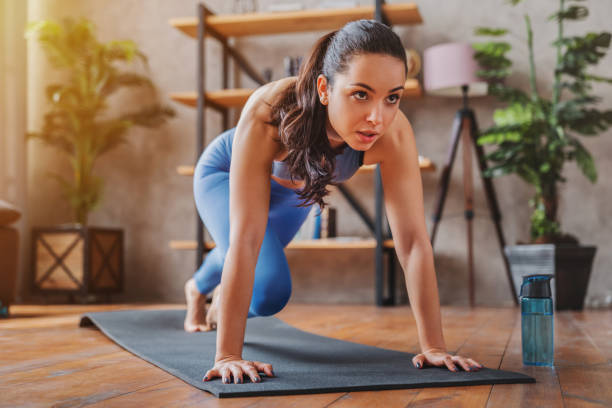 A young athletic woman is on a yoga mat taking a pose. She is looking in front of her with a determined facial expression. Beside her is her water.