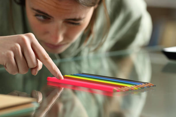 A young woman is closely looking at a set of colored pencils she has put in order. She has one of her eyes closed as she tidies up the stack of pencils.