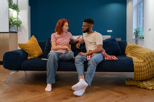 A biracial couple is sitting together on a couch as they talk.