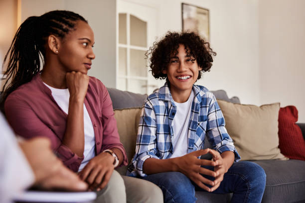 An African American mother is sitting beside her son on the couch as she looks at him and he smiles.