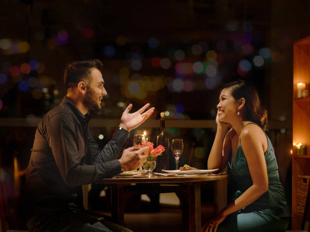 A young biracial couple is at a fancy dinner together in a dark restaurant, sitting across from each other.