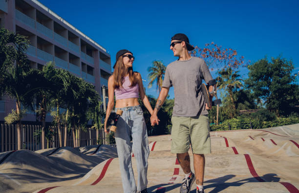 A young American couple is taking a walk outside together. The couple is holding hands as they look at each other and smile.