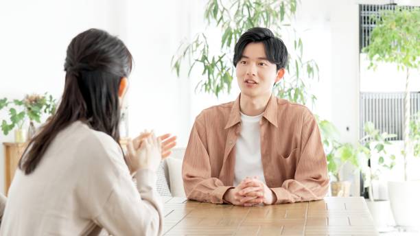 An Asian couple is sitting across one another on the dinner table as they talk.