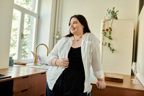 A young woman is standing in her kitchen leaning on the counter as she smiles.