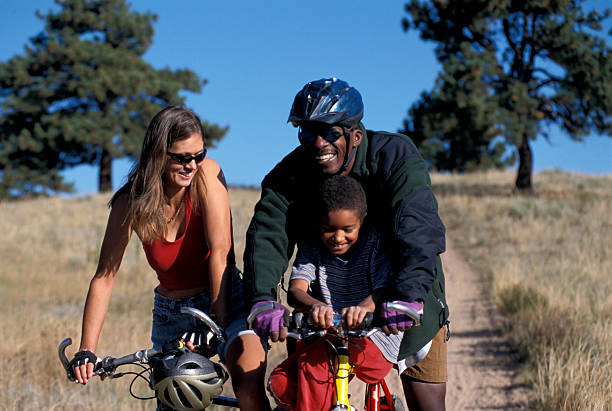 A biracial couple is biking on a trail with their young child side by side.