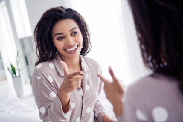 A young African American woman is looking at herself in the mirror, smiling.