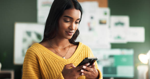 An Indian American woman is looking at her phone in her office.