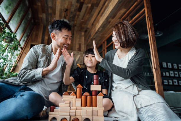 An Asian American couple is sitting with their child in between them playing with blocks. They are all high-fiving each other.