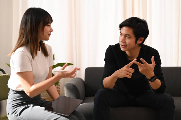 A young Asian American couple is sitting in the living room talking.