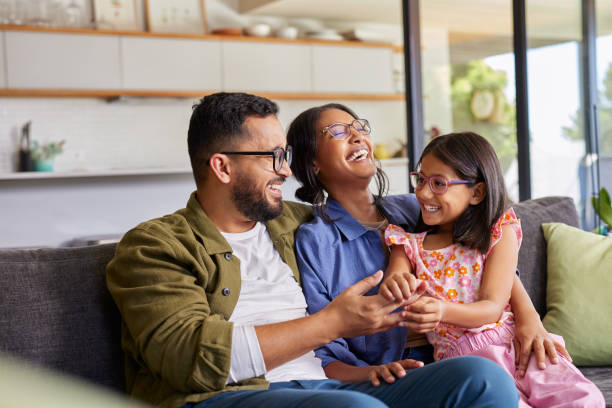 An Indian family of three is sitting in their home on the couch. They are all laughing and sitting close to one another.