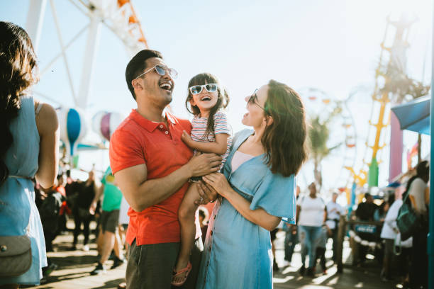 A young family of three is at a fait together. The father is carrying their daughter as they all laugh.